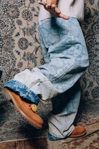 Model wearing Axis Studios Paisley Jeans with full paisley jacquard pattern, cuffed hem showing contrast wash, styled with Timberland boots on ornate rug.