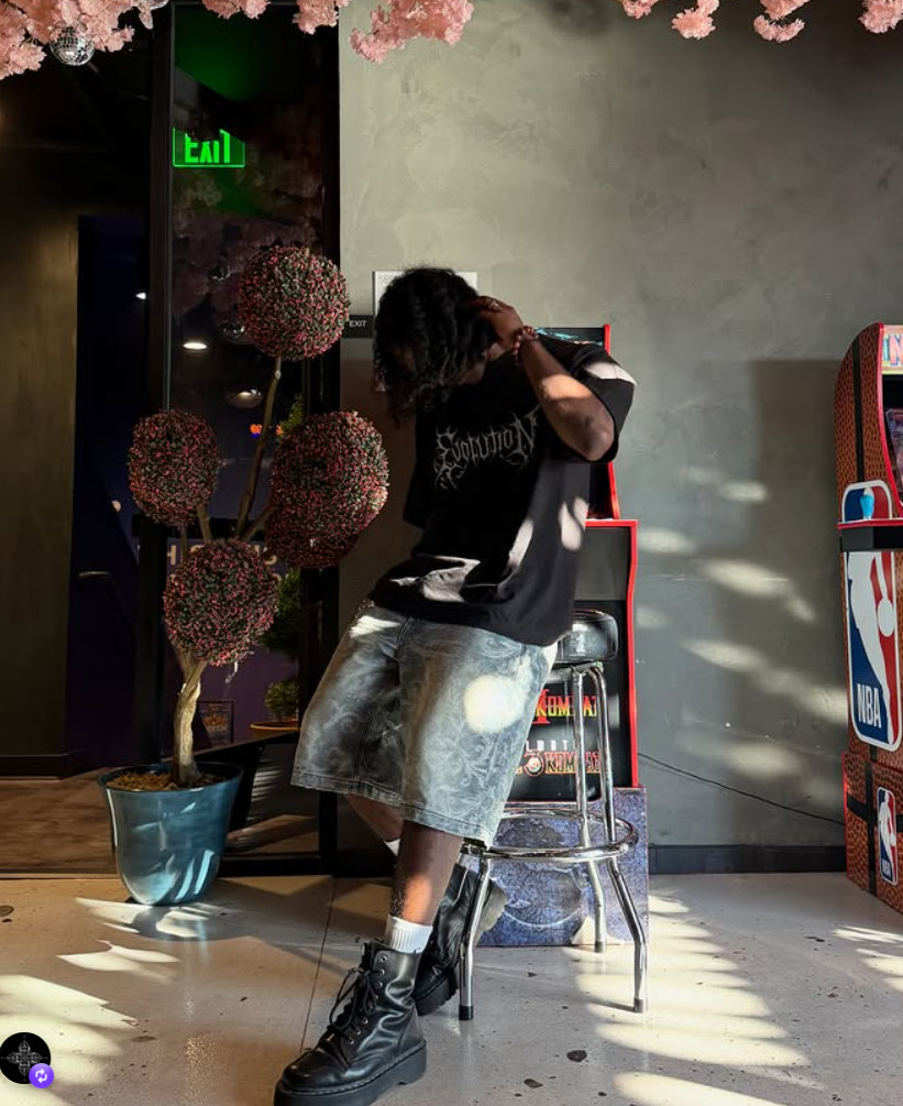 Model wearing Axis Studios Cloud Jorts with cloud jacquard pattern, styled with black tee and boots in an arcade setting.