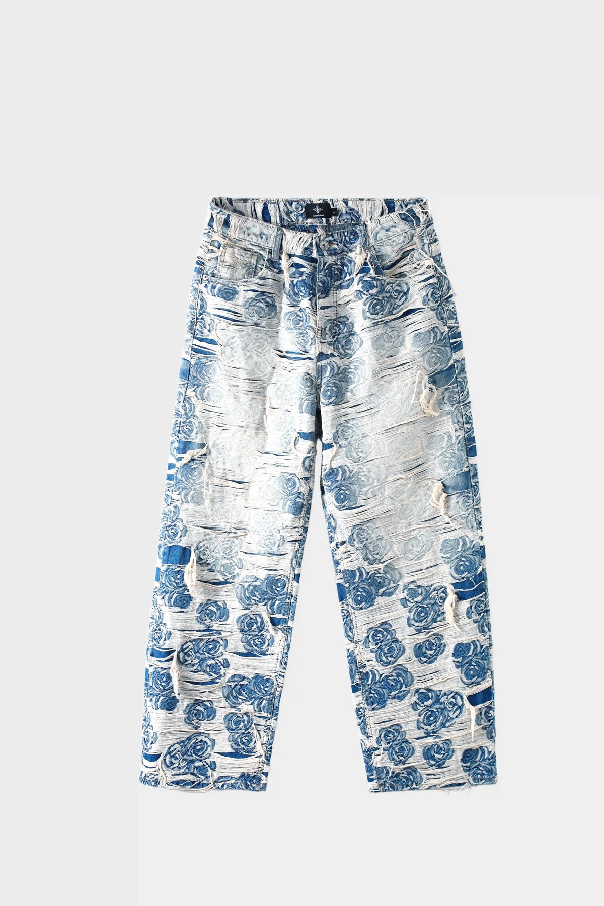 Light blue denim jeans with blue-white porcelain rose jacquard pattern and heavy distressing, wide-leg fit, front view on white background.